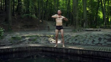 Egzersiz yapan genç adam ellerini ormanda hareket ettiriyor, esneme hareketleri yapıyor, atletizm yapıyor.