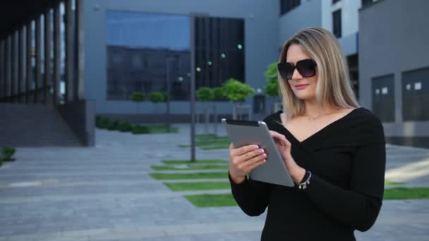 Бізнес-леді в сонцезахисних окулярах, використовуючи цифровий планшет у фінансовому районі — стокове відео