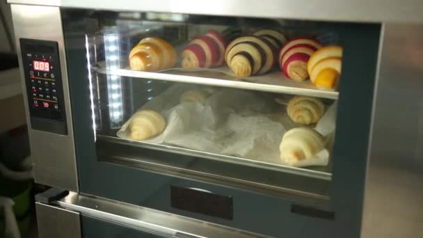 Verse croissants bakken in de oven. Bagel op een muffinlaken wordt gebakken. Bekijk glas — Stockvideo