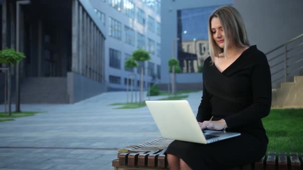 Een oplettende vrouw die op een laptop op straat zit. Zakenvrouw — Stockvideo