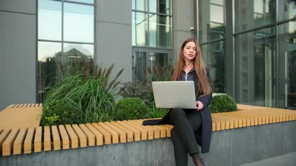 Mujer de negocios utiliza portátil contra edificio de oficinas. Mujer de negocios caucásica — Vídeo de stock