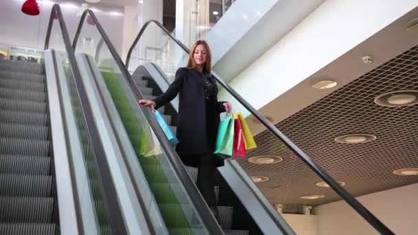 Mujer joven desciende bajando en una escalera mecánica en el centro comercial. Sostenga el papel — Vídeos de Stock