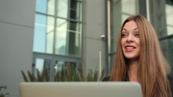 Een conferentie op afstand met een laptop op een bankje in de straat. Gelukkige vrouw — Stockvideo