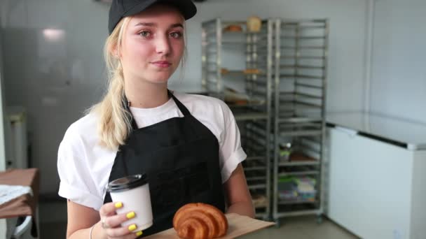 Особа продавця продовжує посміхатися обличчям. Жіночий пекар дає кавовий круасан — стокове відео