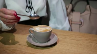 Kaşıklı kapuçinolu kadın elleri, yakın plan. Genç bayan kahve içiyor.