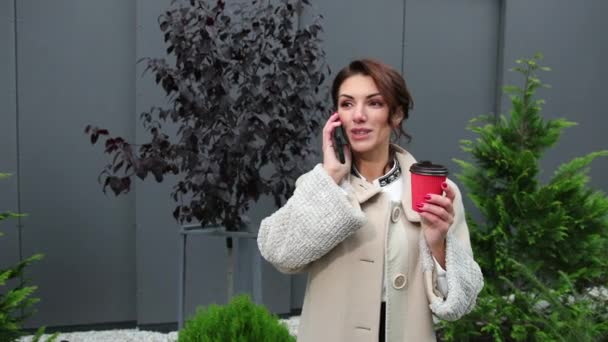 Portrait d'une jolie jeune femme brune utilisant un téléphone portable tenant une tasse de café — Video