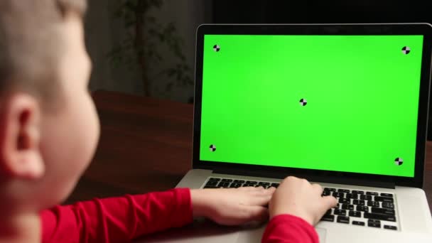 Over de schouder kleine jongen gebruik laptop met groen scherm mock-up op een display. — Stockvideo