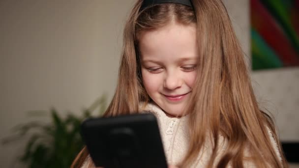 Seorang gadis muda menonton video di smartphone sambil berbaring sofa. Lass mengintip — Stok Video