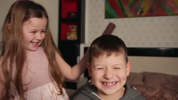 Сестра робить зачіску до брата, чіпляє волосся гребінцем у домашній спальні.. — стокове відео