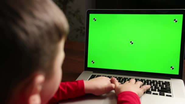 Over de schouder kleine jongen gebruik laptop met groen scherm mock-up op een display. — Stockvideo
