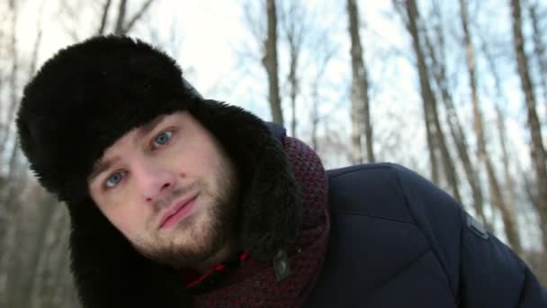雪に覆われた路上の冬の帽子の面白い男の肖像画は、カメラを見て — ストック動画