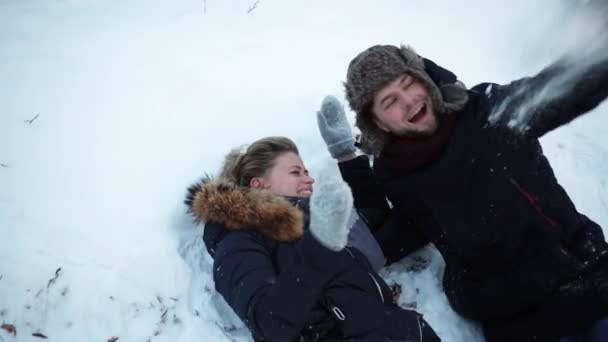 Een meisje en een jongen liggen in de sneeuw, rotzooien, sneeuw gooien, plezier hebben, kindertijd — Stockvideo