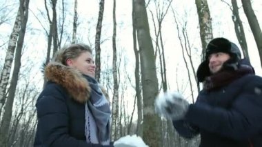 Karla kaplı kış ormanlarında bir kadın ve erkek birbirlerine kar atıyorlar.