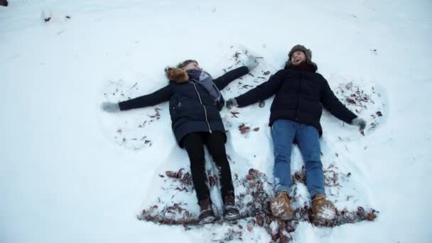 Lány és egy srác feküdt a havon télen. Feküdj a hóban, mozgasd a karjaikat, lábaikat., — Stock videók