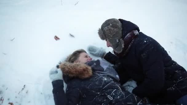 A girl and guy lie in the snow, fool around, throw snow, have fun, childhood — Stock Video