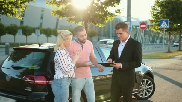 Vendedor vende o carro para jovem casal feliz, assinando contrato com vendedor — Vídeo de Stock