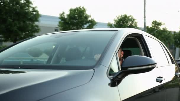 Un jeune homme barbu regarde par la fenêtre de la voiture, sourit et donne les pouces vers le haut — Video