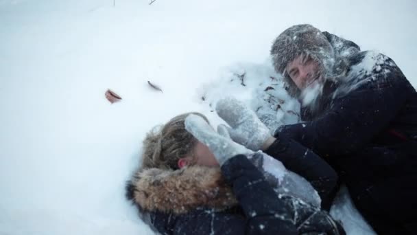 Egy lány és egy srác fekszenek a hóban, bolondoznak, havat dobálnak, szórakoznak, gyerekkorukban — Stock videók