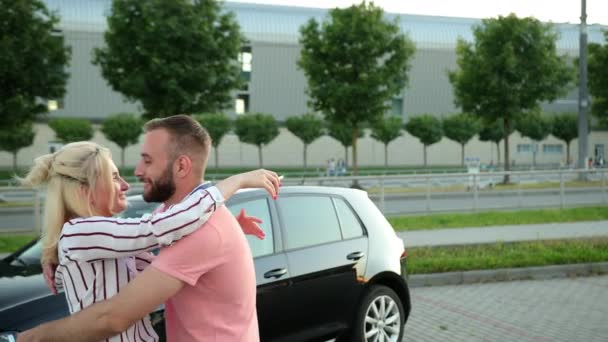 Mujer abraza al hombre con sus manos y sostiene las llaves del coche. Hay un vehículo — Vídeo de stock