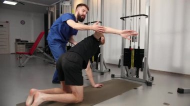 Hastanedeki spor salonunda genç bir adama yardım eden fizyoterapist. Yassı kişi