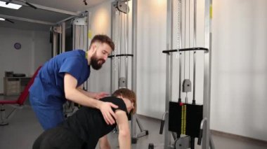 Hastanedeki spor salonunda genç bir adama yardım eden fizyoterapist. Yassı kişi