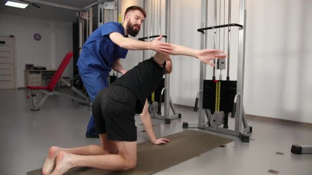 Fysiotherapeut assisteert jongeman in de sportschool in het ziekenhuis. Persoon mager — Stockvideo