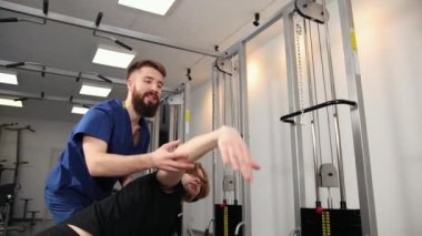 Fizyoterapist, esneme egzersizleri yapan genç adama spor salonu hastanesinde yardım ediyor..