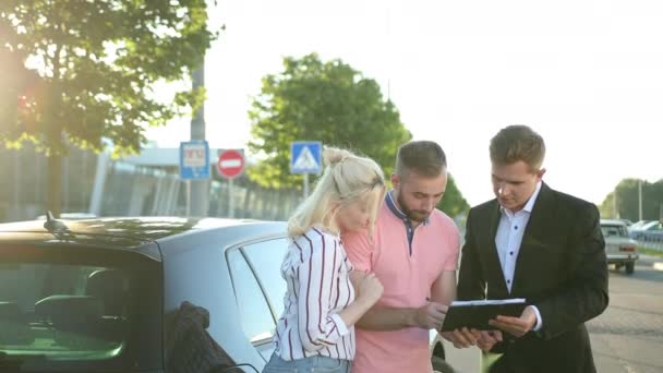 Seller sells the car to happy young couple. Buyer sign a vehicle purchase — Stock Video