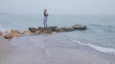 Kayalık sahilde sonbaharda deniz manzarasının tadını çıkaran genç bir kadın. Güzel manzara