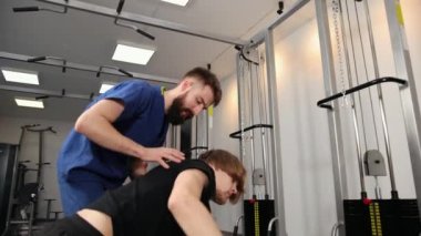 Hastanedeki spor salonunda genç bir adama yardım eden fizyoterapist. Yassı kişi