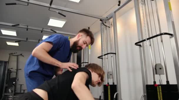 Physical therapist assisting young man in the gym at hospital. Person lean — Stock Video