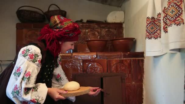 Jovem mulher em um traje tradicional ucraniano vyshyvanka coloca massa de pão crua — Vídeo de Stock