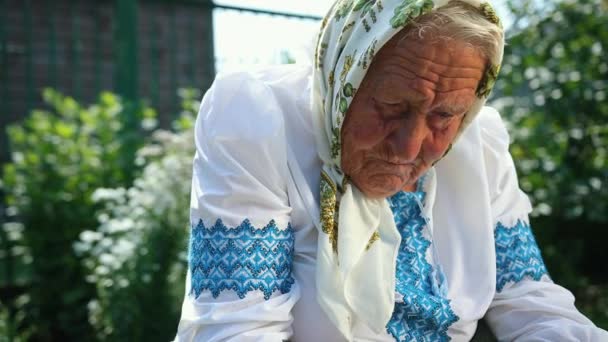 An old grandmother is sitting on the street and reading a book. Vyshyvanka — Stock Video