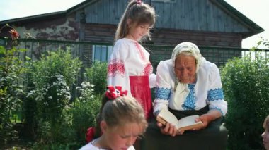 Yaşlı bir büyükanne sokakta oturuyor ve bir kitap okuyor. Kızlar dinleyin.