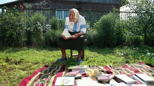 Une vieille grand-mère est assise dans la rue et lit un livre. Vyshyvanka. — Video