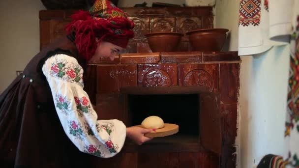 Egy fiatal nő hagyományos ukrán vyshyvanka jelmezben nyers kenyeret tesz a tésztába. — Stock videók