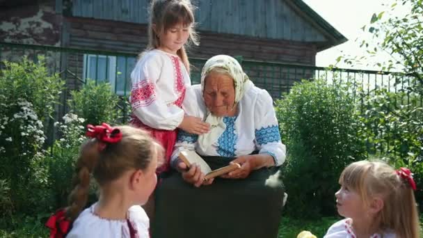 Yaşlı bir büyükanne sokakta oturuyor ve bir kitap okuyor. Kızlar dinleyin. — Stok video