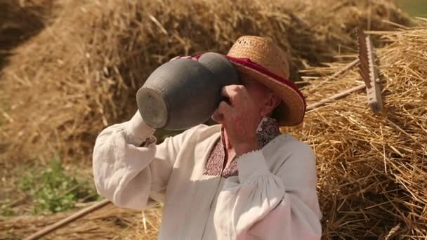 Thirsty old man grandpa drinks water from jug. Male in straw hat is tired labor — Stock Video