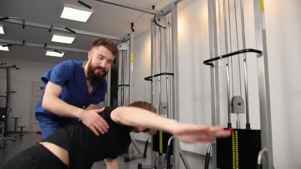 Fisioterapeuta ayudando a un joven con ejercicios de estiramiento gimnasio hospital. — Vídeo de stock