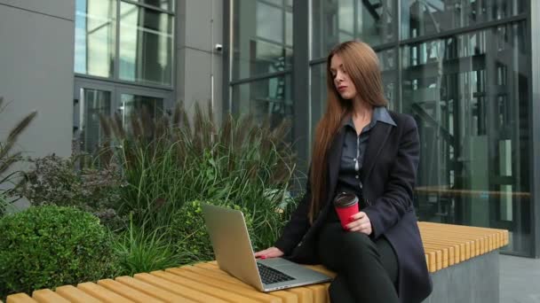 Een vrouw die over een onderwerp nadenkt. Aantrekkelijk bruin haar met behulp van laptop buiten. — Stockvideo