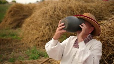 Yaşlı susamış büyükbaba sürahide su içiyor. Hasır şapkalı bir erkek yorgun işçidir.