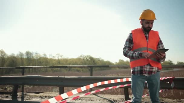 Ung skäggig man inspektör i orange väst och skyddshjälm med tablett — Stockvideo