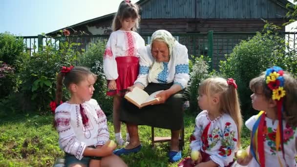Yaşlı bir büyükanne sokakta oturuyor ve bir kitap okuyor. Kızlar dinleyin. — Stok video