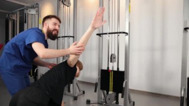 Fizyoterapist, esneme egzersizleri yapan genç adama spor salonu hastanesinde yardım ediyor..