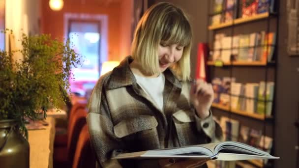 Portret mądrego ucznia z otwartą książką czytającego ją w bibliotece uniwersyteckiej. Kobieta. — Wideo stockowe