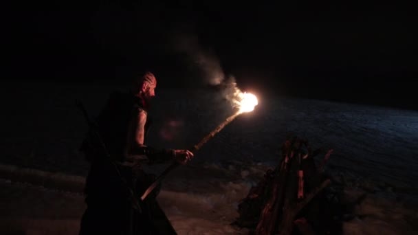 Wikinger mit einer Fackel entzündet Lagerfeuer. Brutaler männlicher Krieger mit gefährlichem Aussehen am Feuer. — Stockvideo