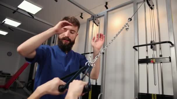 Концепція реабілітації. Молодий чоловік виконує вправи під фізіотерапевтом — стокове відео