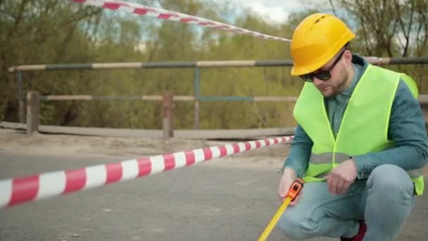 Engenheiro barbudo em fita métrica protetora capacete nas mãos mede distância — Vídeo de Stock