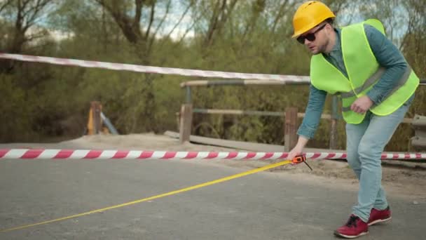 Bearded engineer in protective helmet tape measure in hands measures distance — Stock Video