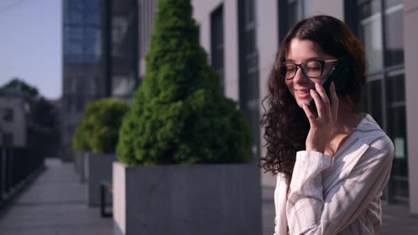 Schöne brünette junge Frau mit Brille spricht Handy trinken — Stockvideo